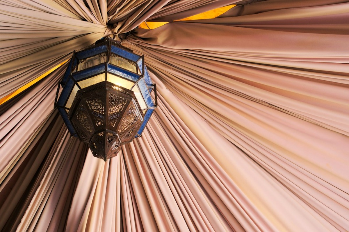 Art-deco styled hall with a draped backdrop, warm uplighting and set tables before guests arrive